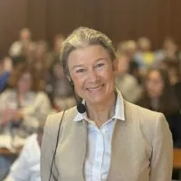 Hanne Skaarberg Holen står ved mikrofon i foredragssal, med publikum sittende uklart i bakgrunnen.